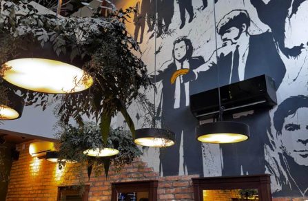 Mural em dois andares na Barbearia Tarantino com pinturas que celebram os filmes clássicos e personagens marcantes de Quentin Tarantino.
